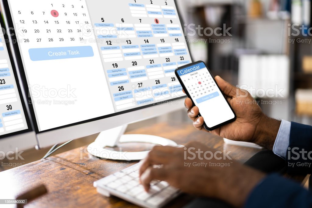 Una persona mirando un calendario en línea en una computadora de escritorio y un teléfono.